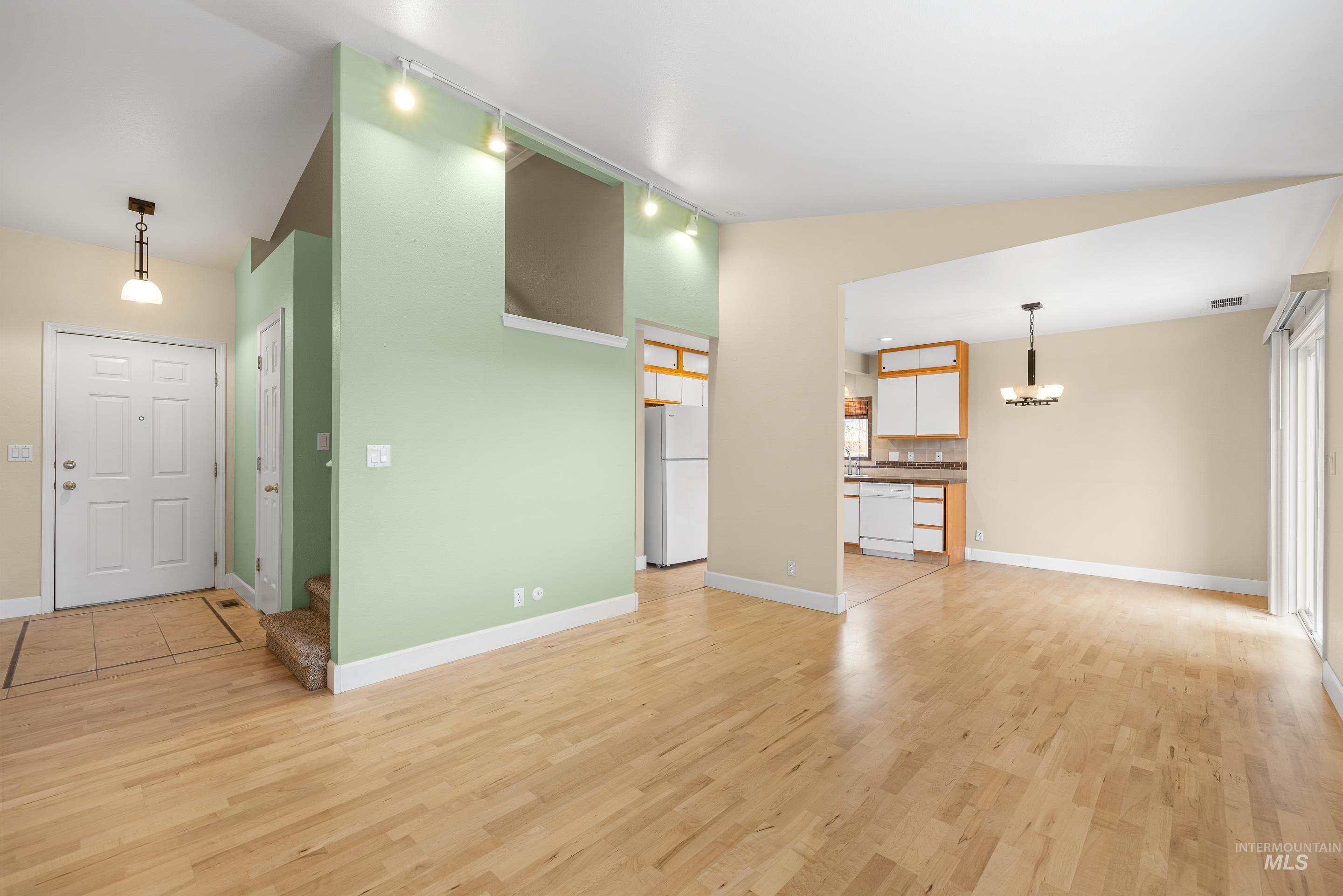 Unfurnished living room featuring vaulted ceiling, light wood-style flooring, and suspended lighting
