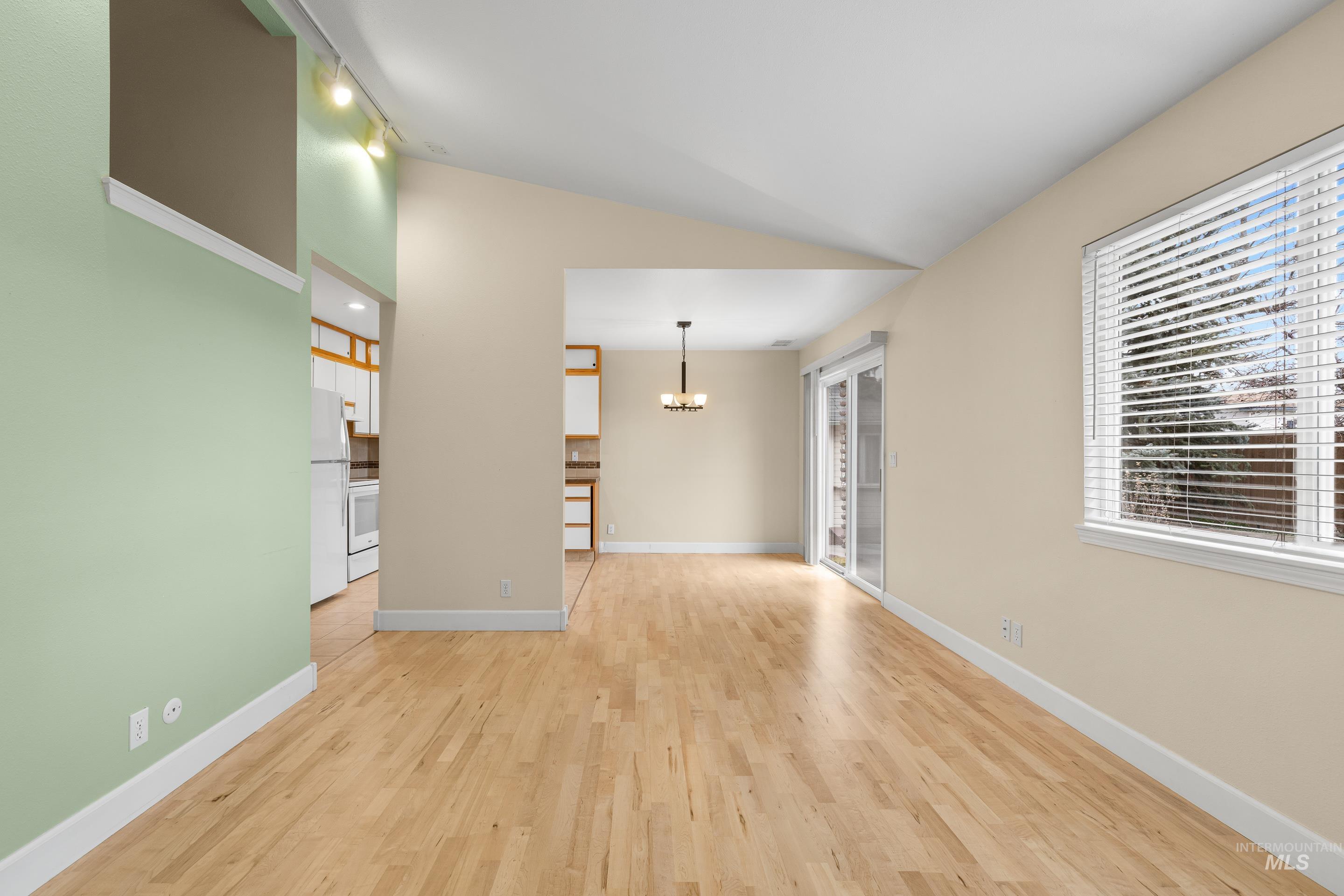 Unfurnished room featuring vaulted ceiling, light wood finished floors, and a chandelier