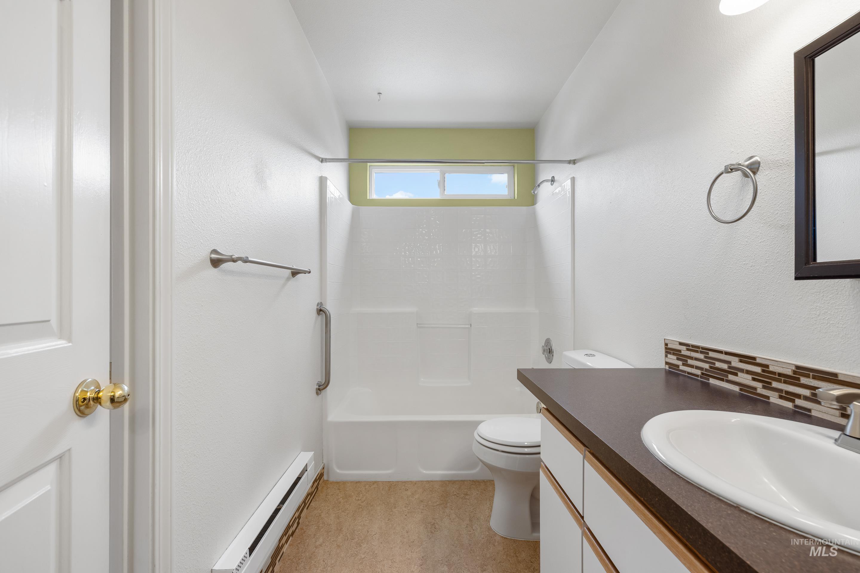 Bathroom featuring vanity, baseboard heating,  shower combination, and backsplash