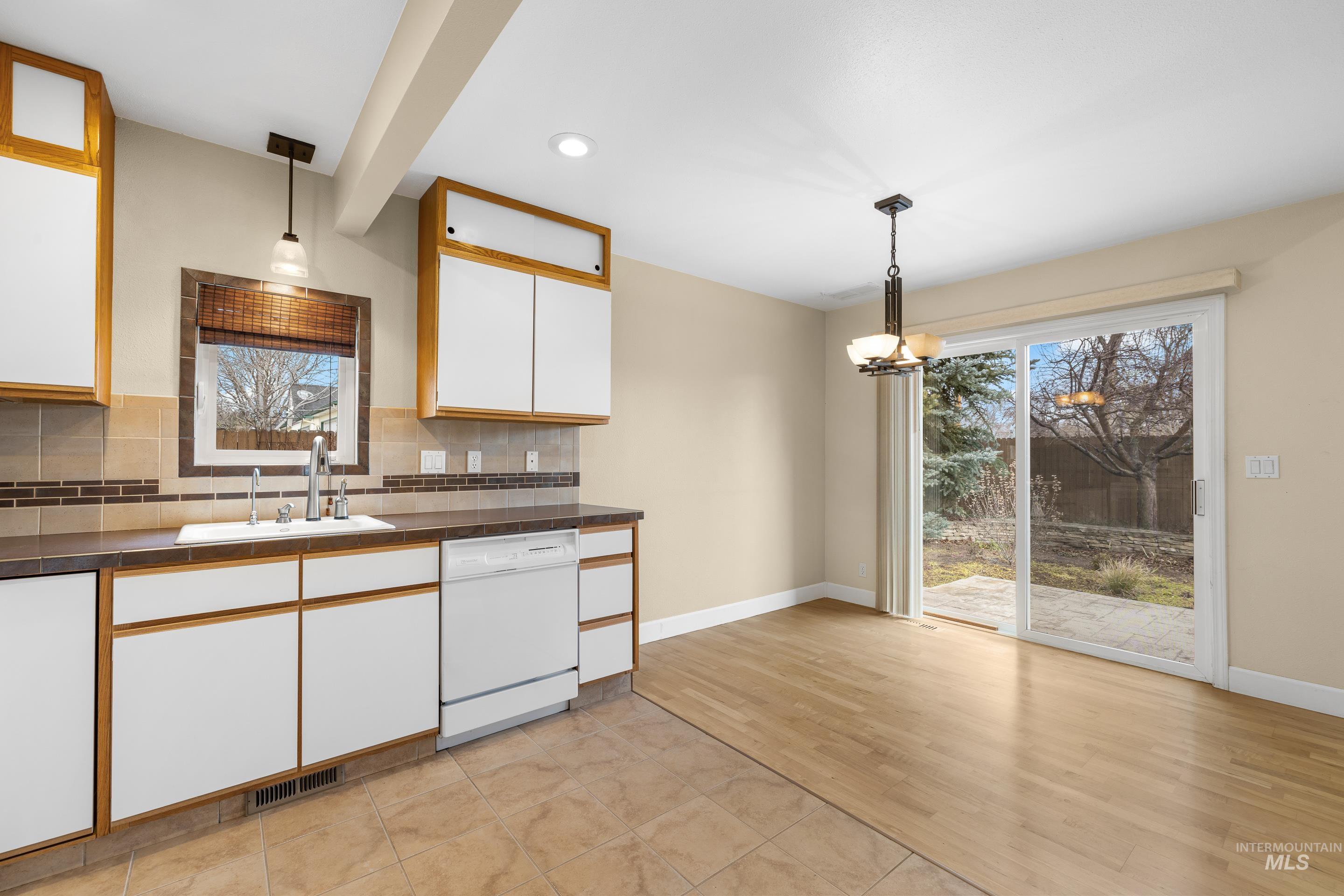 Two tone kitchen featuring dual tone cabinetry, backsplash, dark countertops, dishwasher, and suspended lighting