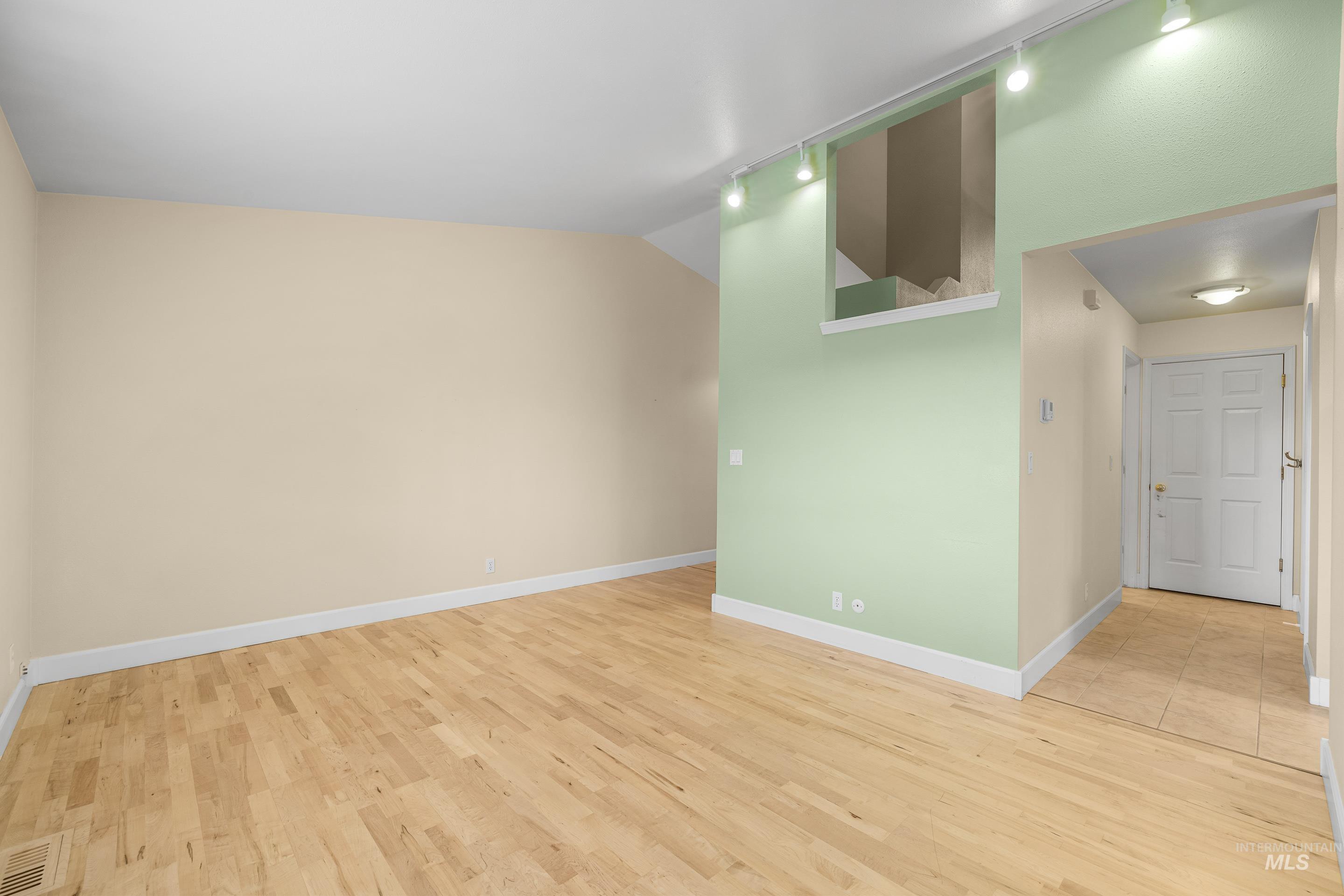 Unfurnished room featuring light wood-style flooring, vaulted ceiling, and track lighting