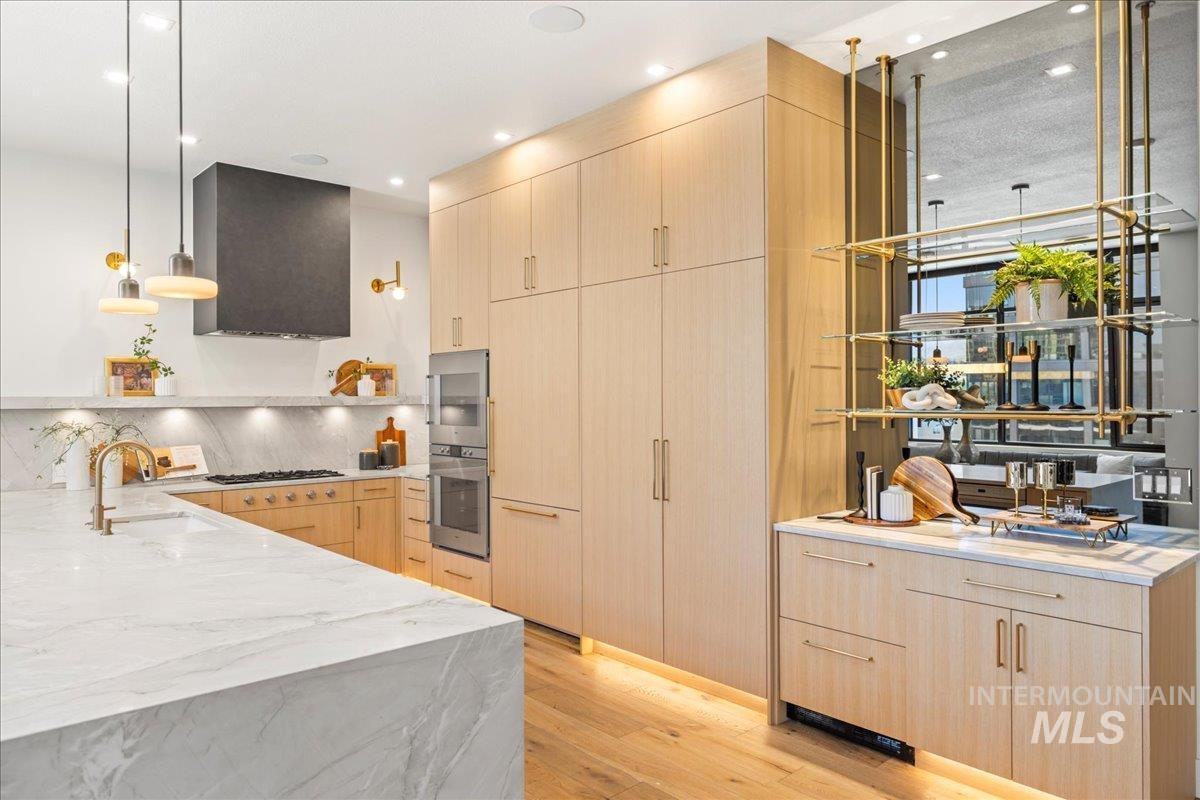 Kitchen with light brown cabinetry, range hood, light stone countertops, light wood-style flooring, and gas cooktop