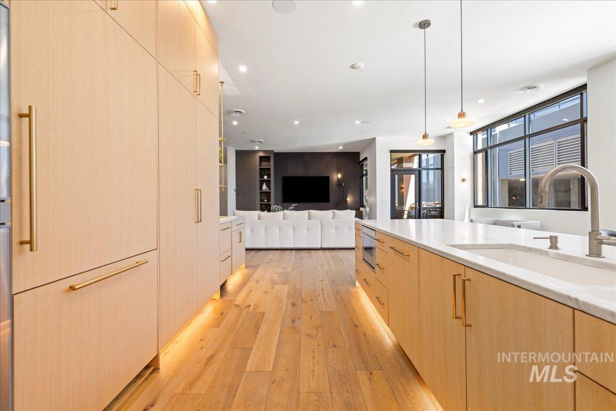 Kitchen with light brown cabinetry, light wood-style floors, modern cabinets, pendant lighting, and open floor plan