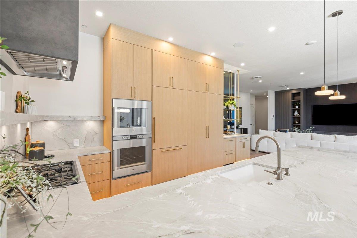 Kitchen featuring light brown cabinetry, decorative backsplash, light stone countertops, range hood, and recessed lighting