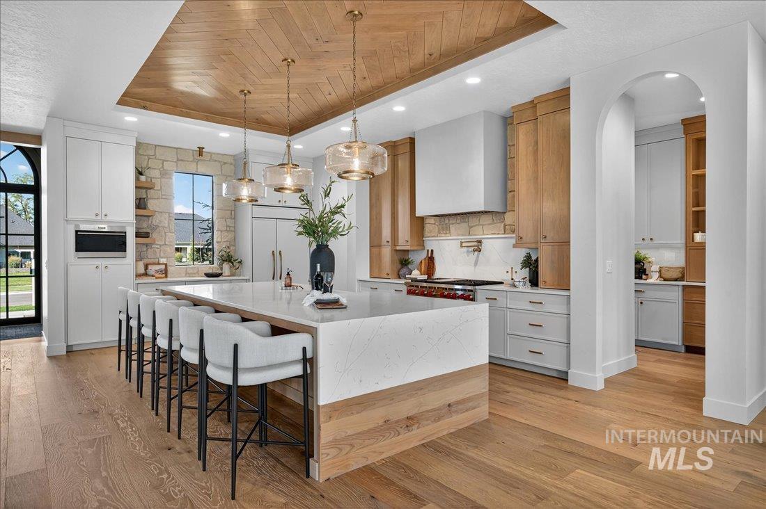 Kitchen with a tray ceiling, a kitchen breakfast bar, open shelves, pendant lighting, and light stone countertops