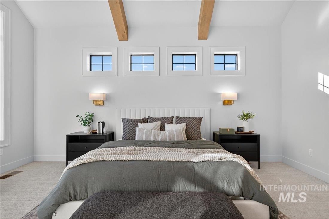 Carpeted bedroom featuring beam ceiling and multiple windows