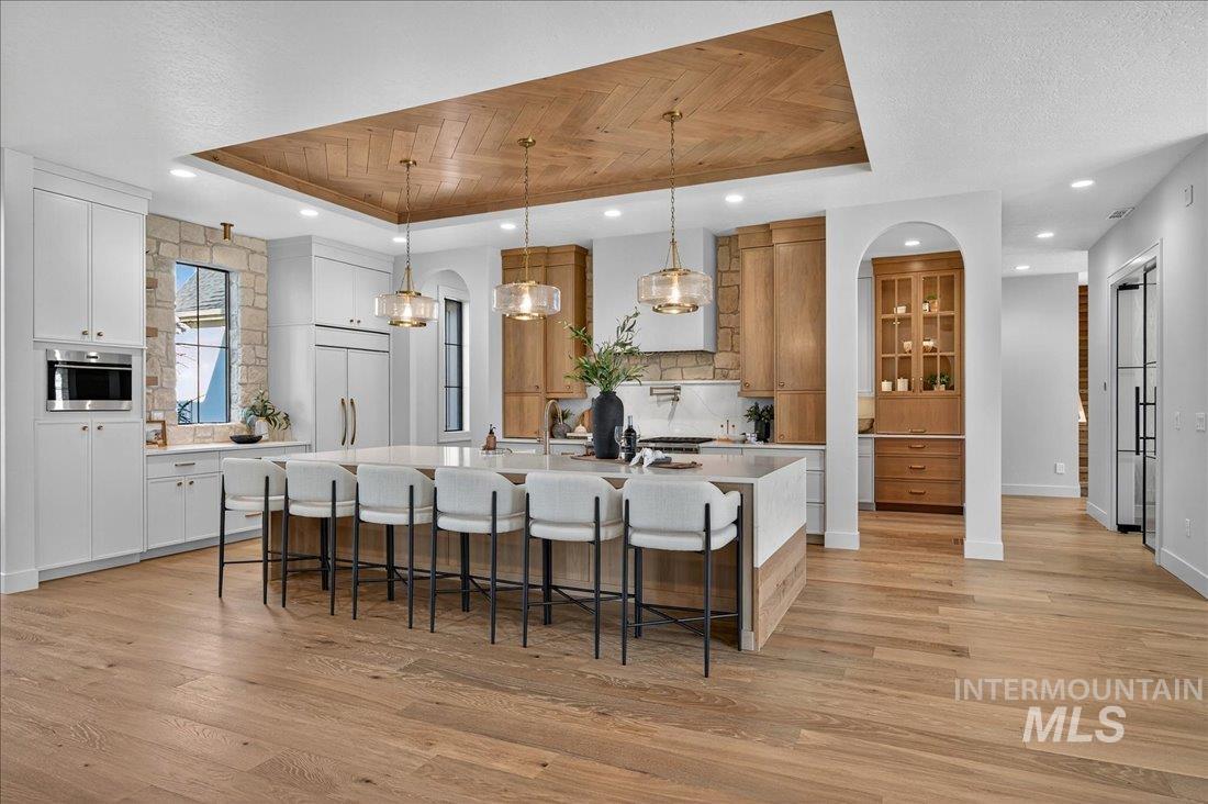 Kitchen featuring a tray ceiling, a breakfast bar, decorative backsplash, a large island with sink, and decorative light fixtures