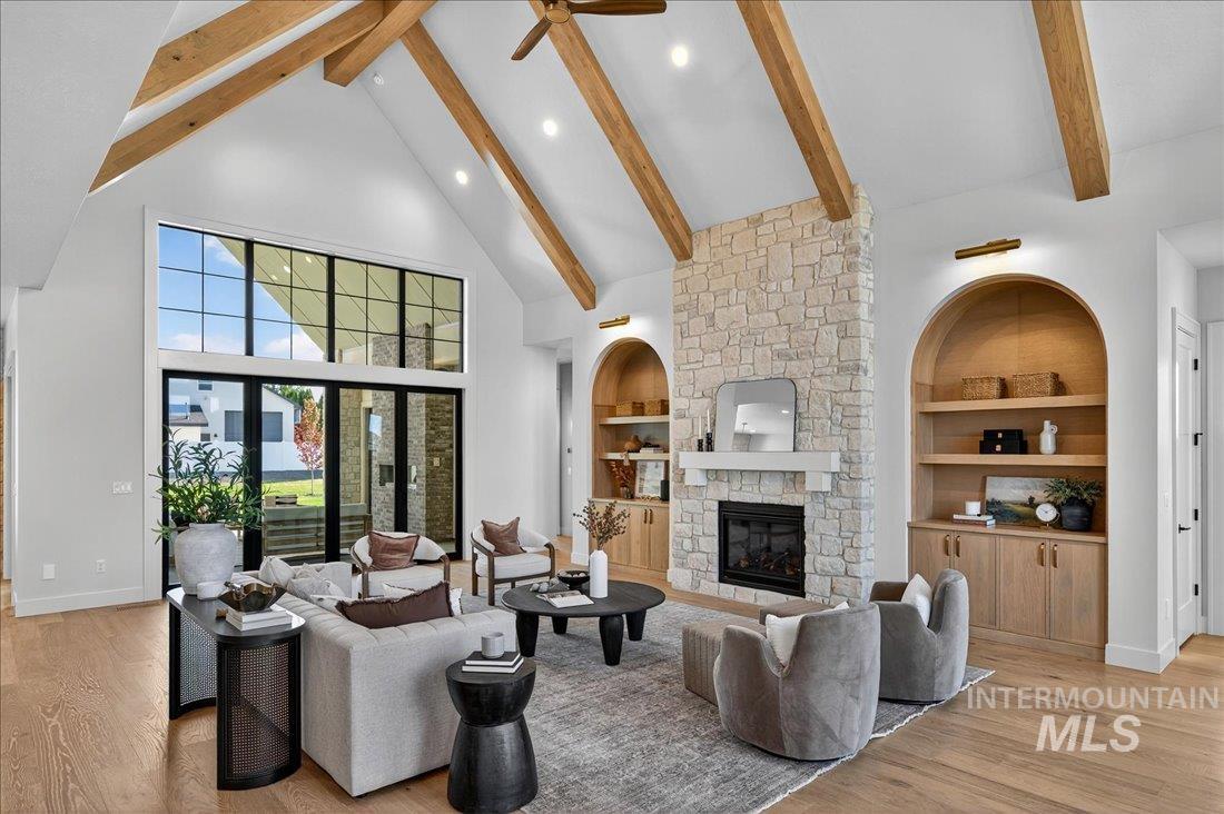 Living room with high vaulted ceiling, beam ceiling, light wood-style flooring, built in shelves, and a fireplace