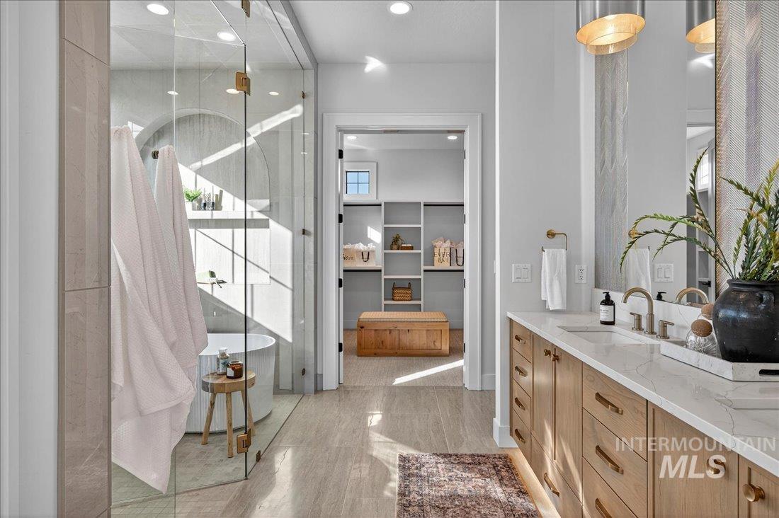 Bathroom with double vanity, a shower stall, a freestanding tub, a walk in closet, and recessed lighting