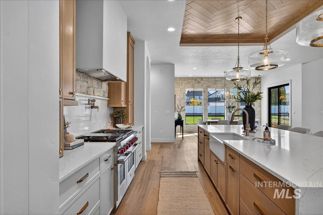 Kitchen with light stone countertops, light wood-style flooring, double oven range, backsplash, and custom exhaust hood