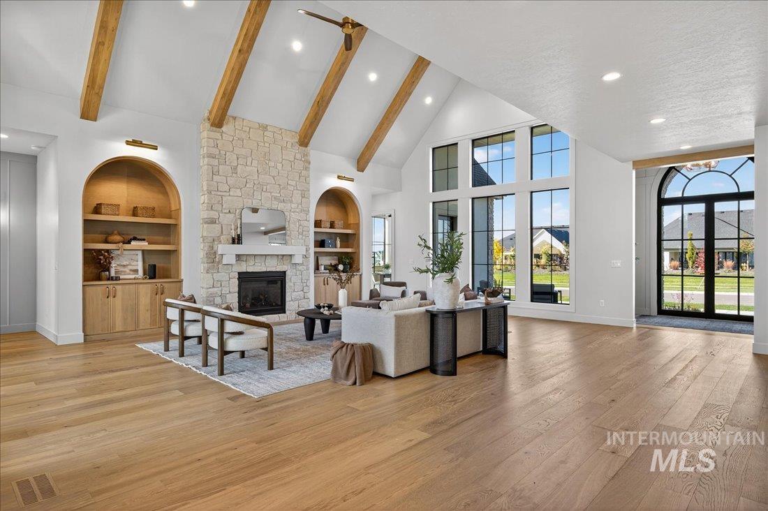 Living area with high vaulted ceiling, built in features, a fireplace, light wood finished floors, and beam ceiling