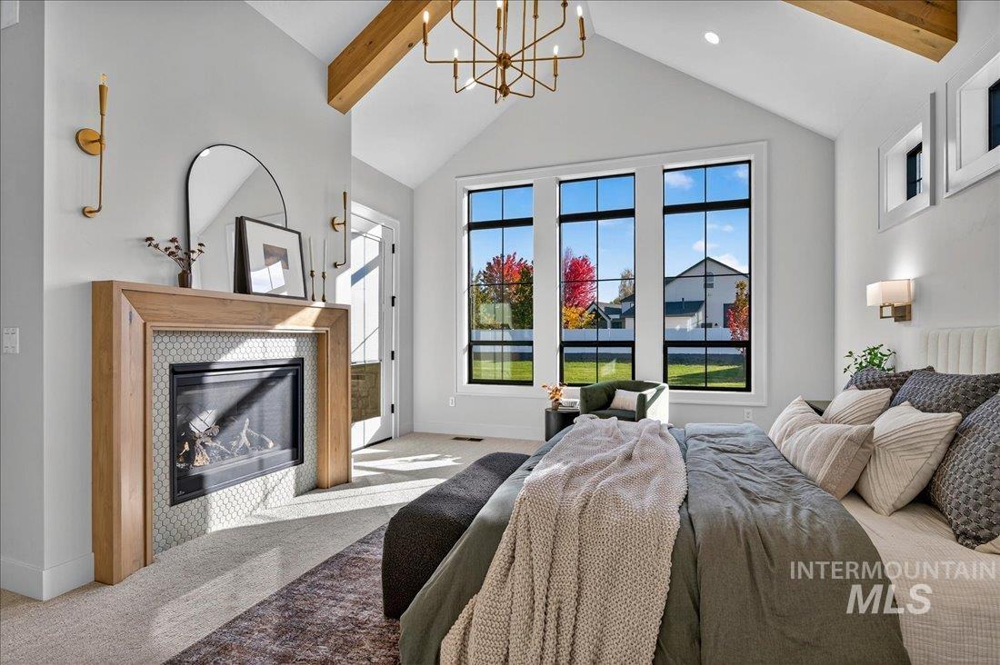 Carpeted bedroom with beamed ceiling, a glass covered fireplace, high vaulted ceiling, and a chandelier