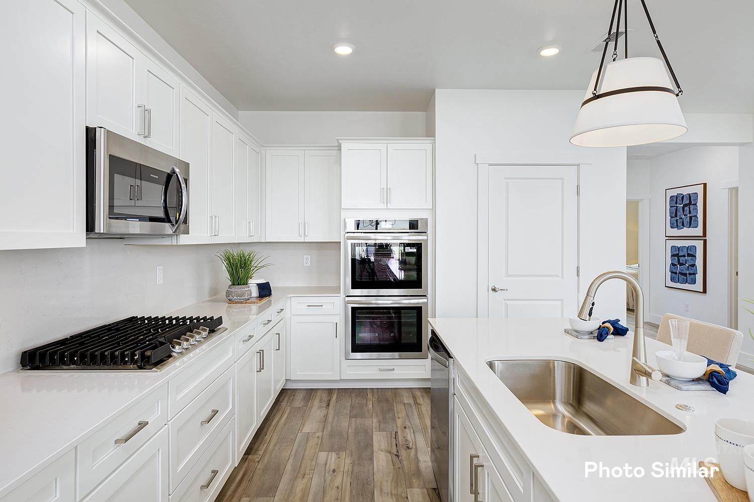 Kitchen with white cabinets, appliances with stainless steel finishes, light wood-style flooring, pendant lighting, and light stone countertops