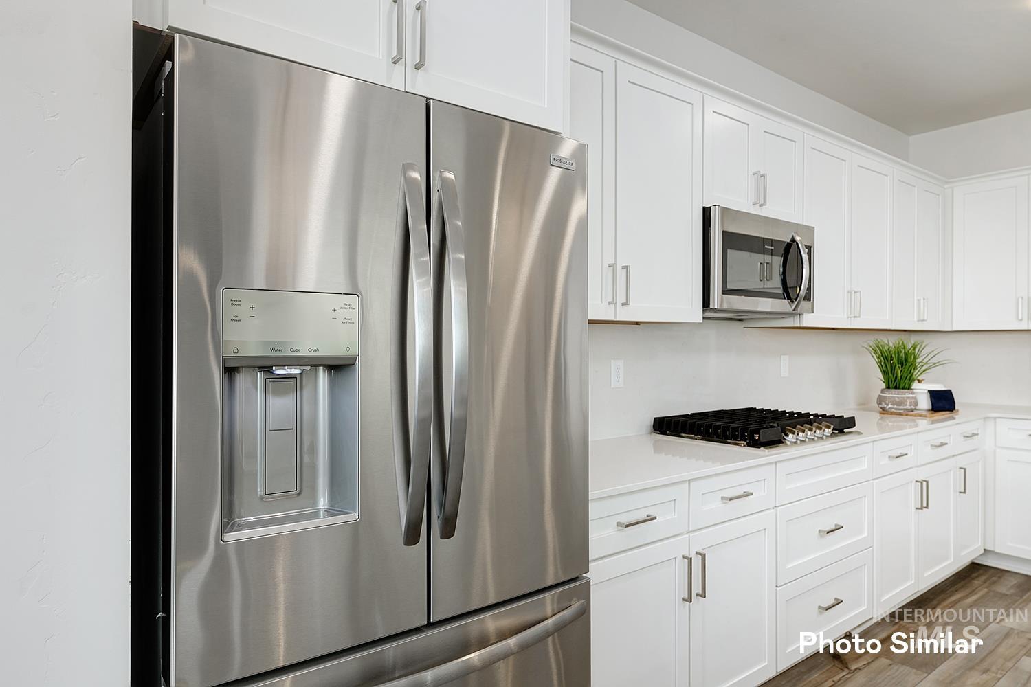 Kitchen with stainless steel appliances, white cabinetry, dark wood-type flooring, and light stone counters