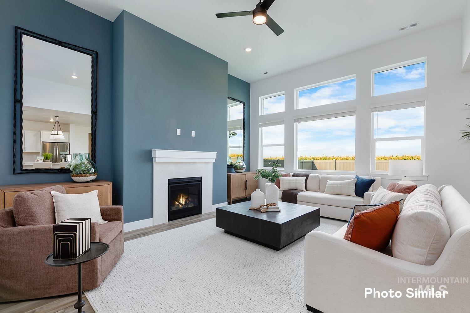 Living room with a glass covered fireplace, wood finished floors, ceiling fan, recessed lighting, and a towering ceiling