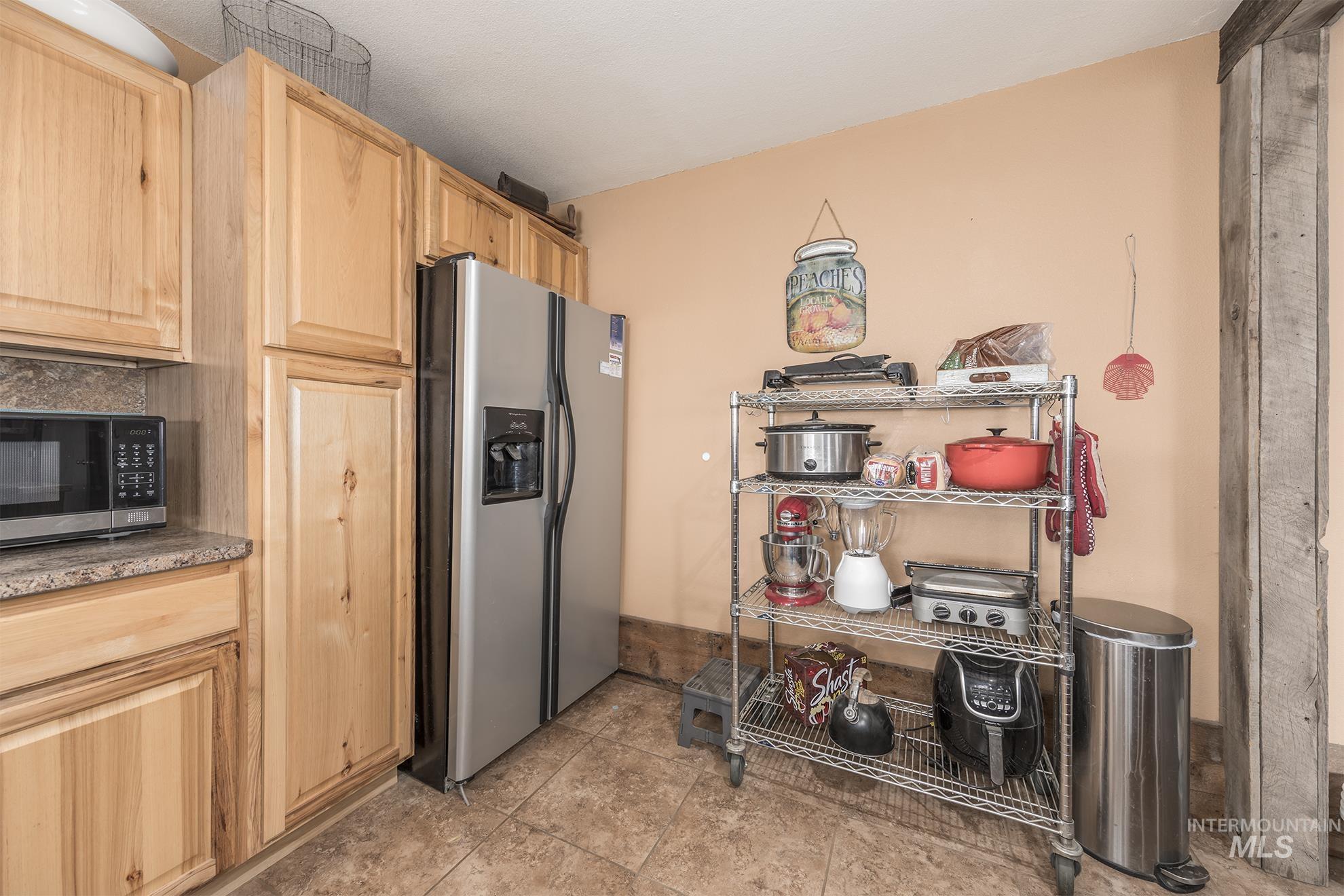 Kitchen with light brown cabinets, appliances with stainless steel finishes, light tile patterned flooring, and tasteful backsplash