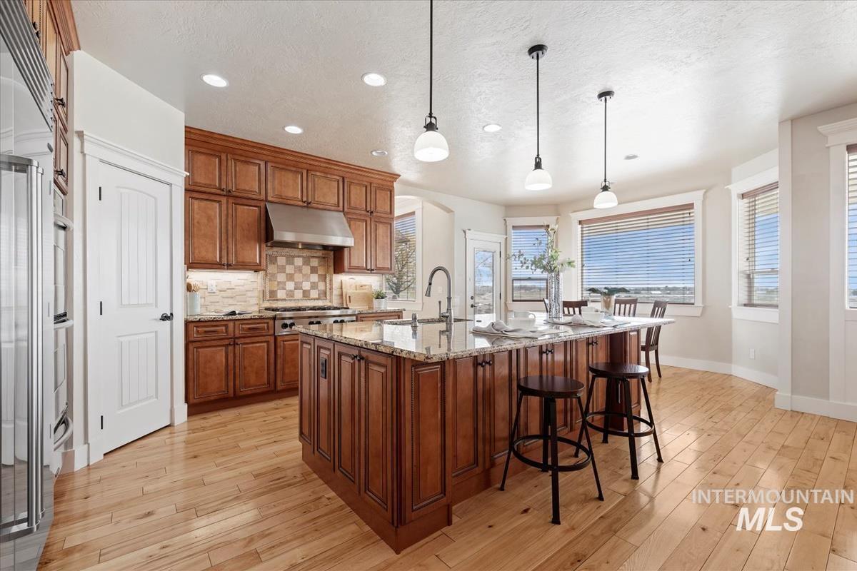 Kitchen with hanging light fixtures, brown cabinets, light stone counters, decorative backsplash, and a textured ceiling