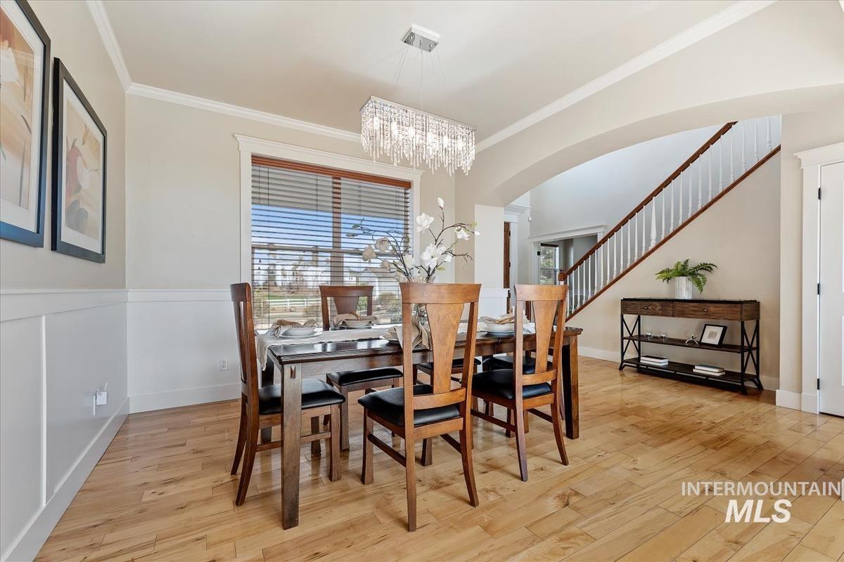 Dining space with ornamental molding, light wood-style flooring, arched walkways, and stairway