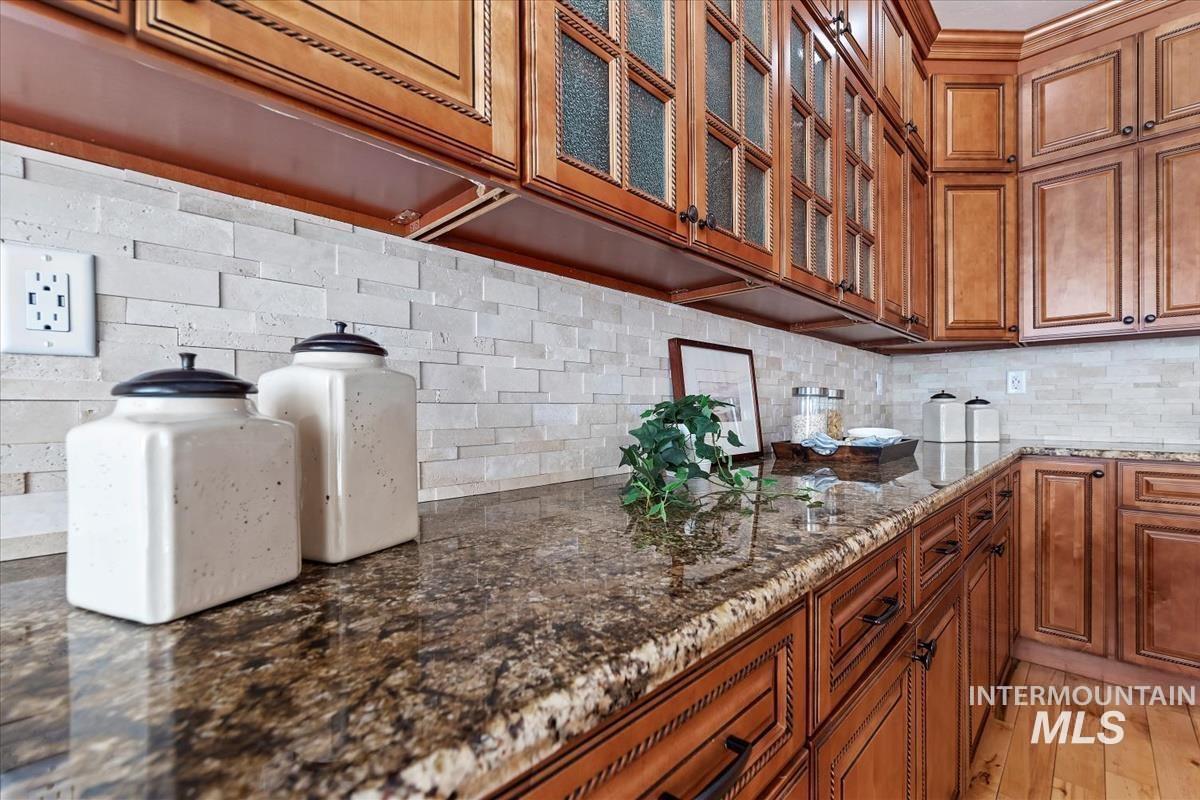 Kitchen with brown cabinets, dark stone countertops, tasteful backsplash, and glass insert cabinets