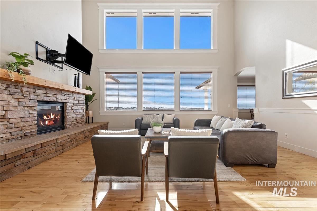 Living room featuring light wood-type flooring, a fireplace, a towering ceiling, and healthy amount of natural light