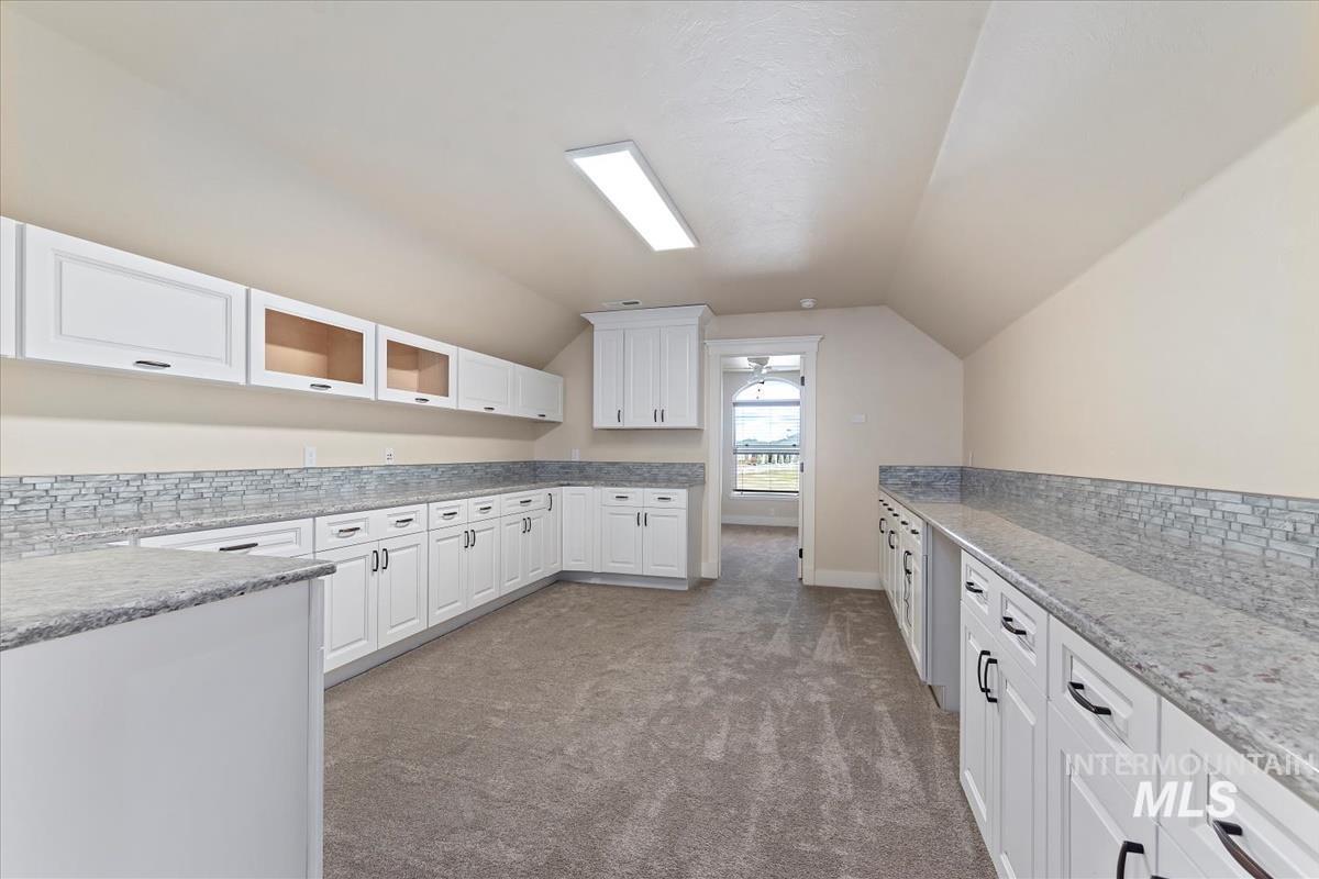 Kitchen featuring white cabinets, light stone countertops, dark carpet, vaulted ceiling, and glass insert cabinets