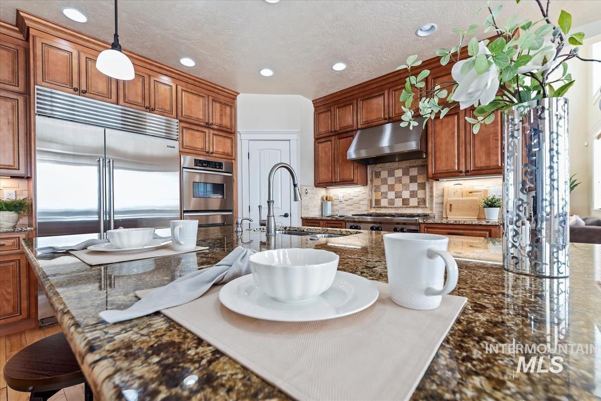 Kitchen featuring dark stone counters, tasteful backsplash, brown cabinets, hanging light fixtures, and a kitchen breakfast bar