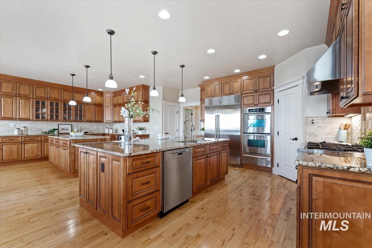 Kitchen featuring brown cabinets, decorative backsplash, a large island with sink, light stone counters, and appliances with stainless steel finishes