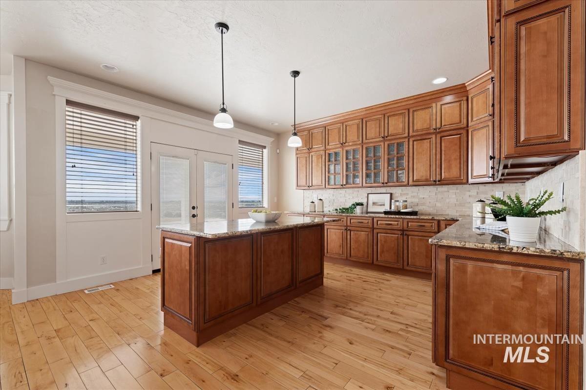 Kitchen with tasteful backsplash, brown cabinets, light stone counters, pendant lighting, and french doors