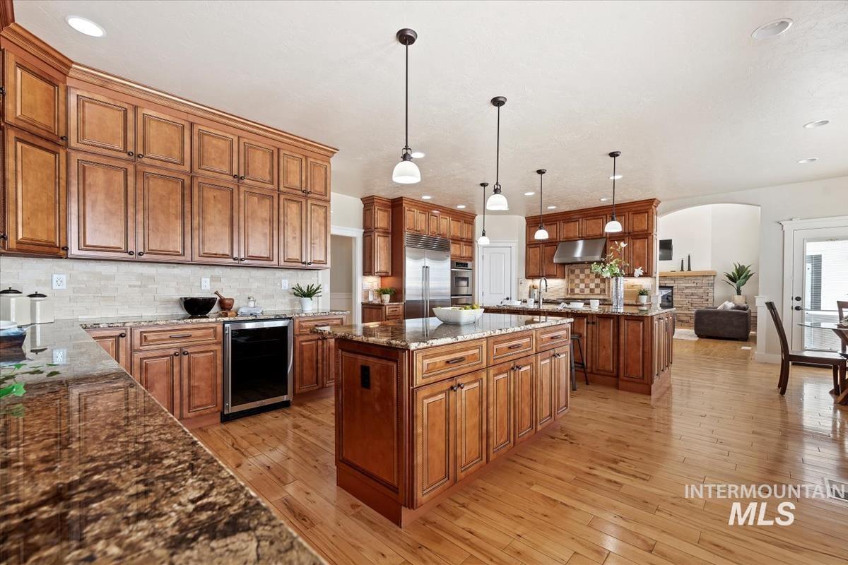 Kitchen with brown cabinetry, dark stone counters, backsplash, decorative light fixtures, and light wood-style floors
