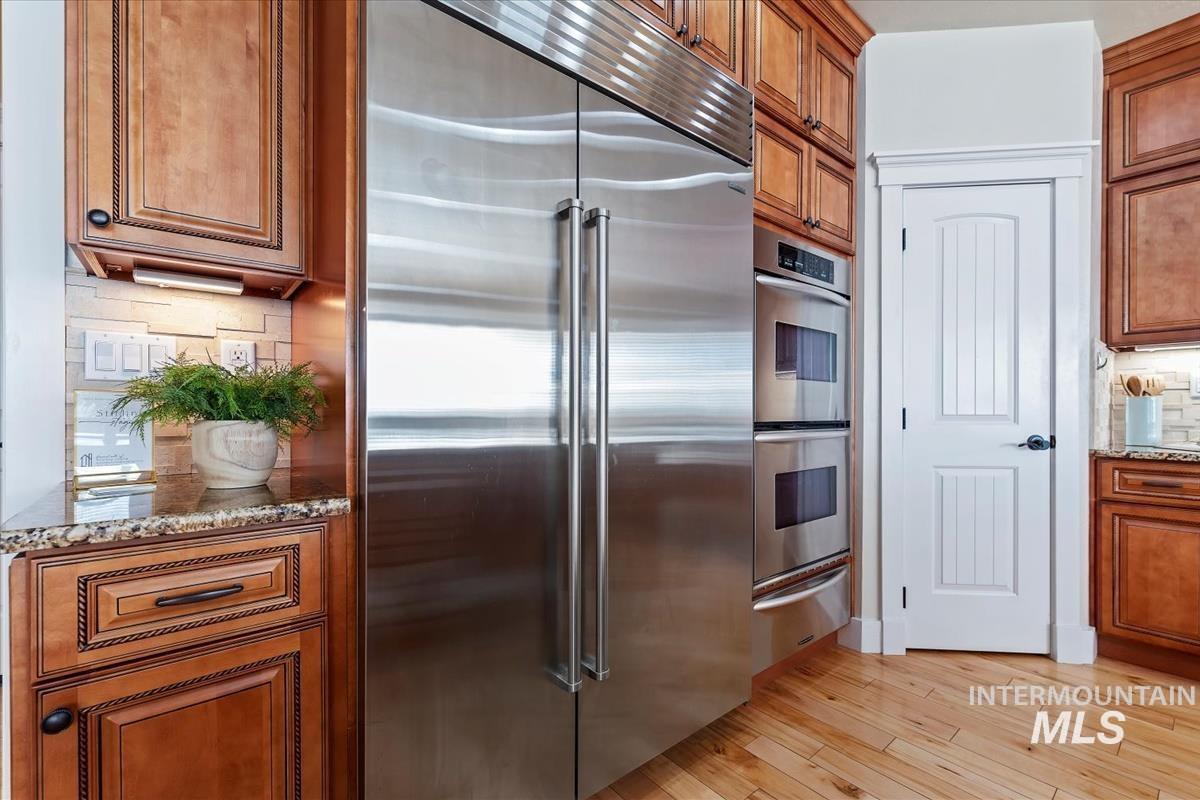 Kitchen featuring tasteful backsplash, brown cabinets, appliances with stainless steel finishes, light stone counters, and light wood-style flooring