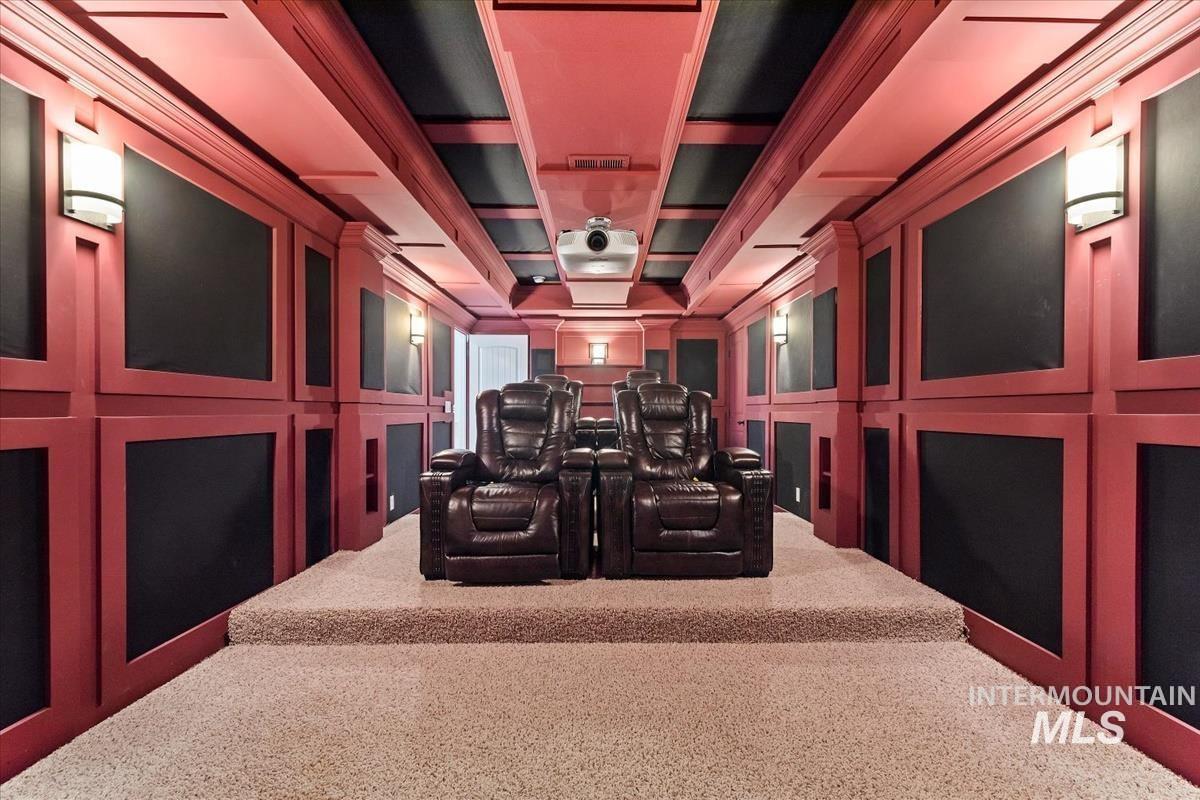 Carpeted home theater with coffered ceiling, a decorative wall, and beamed ceiling