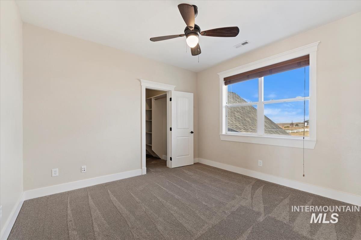 Unfurnished bedroom featuring carpet floors, a spacious closet, and a ceiling fan
