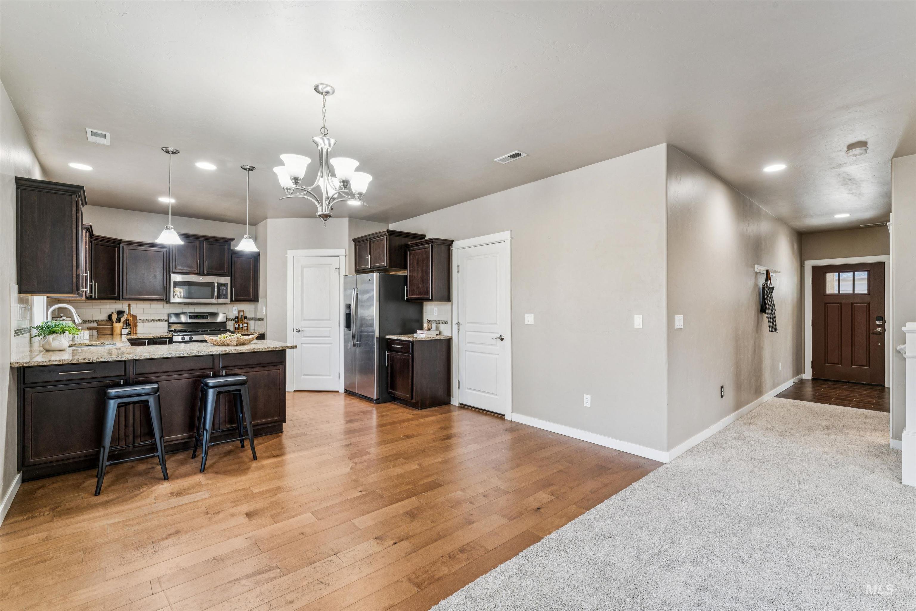 Kitchen with decorative light fixtures, dark brown cabinets, a chandelier, light wood finished floors, and backsplash