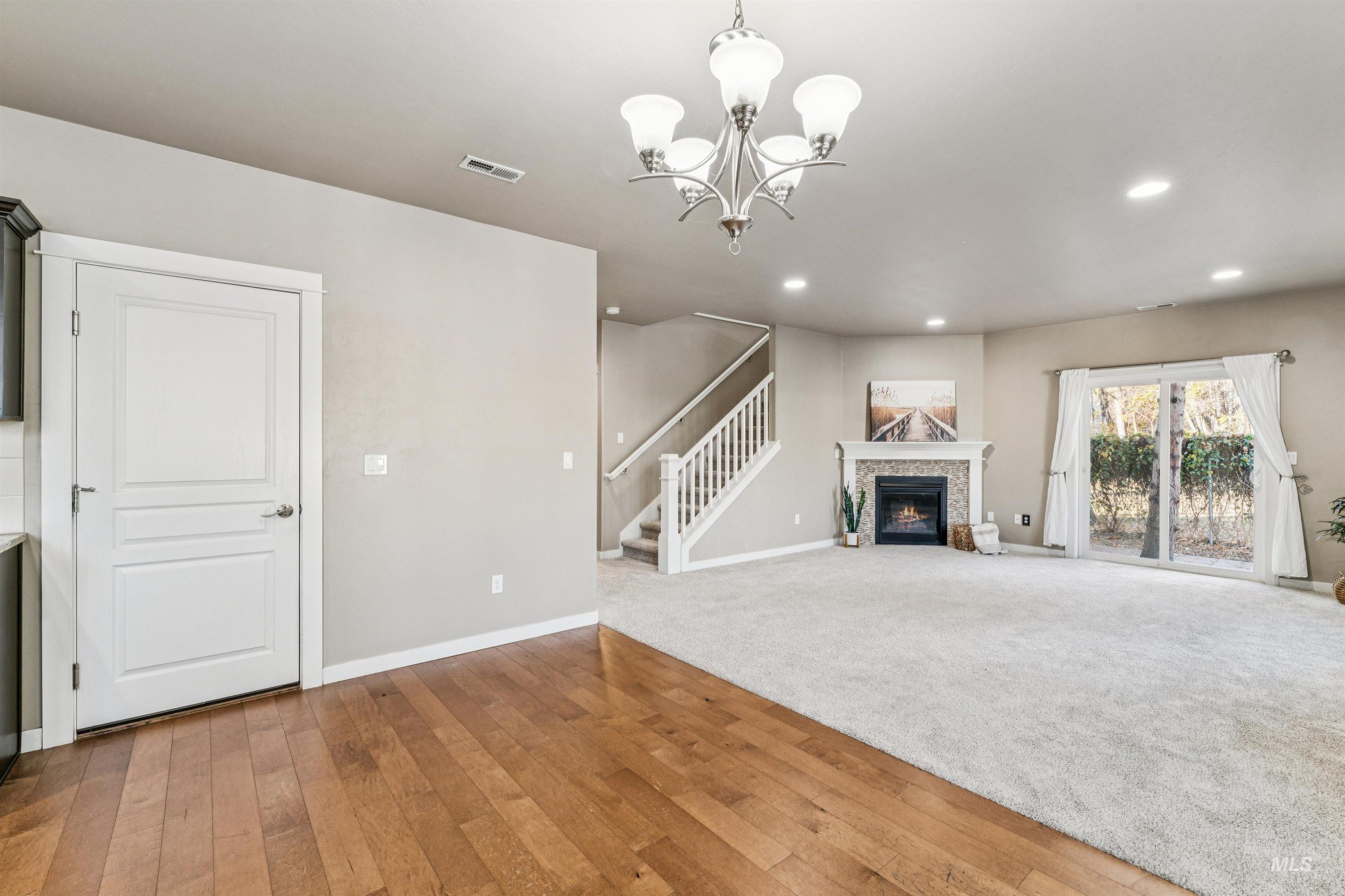 Unfurnished living room with light wood-style floors, a glass covered fireplace, recessed lighting, stairs, and a chandelier