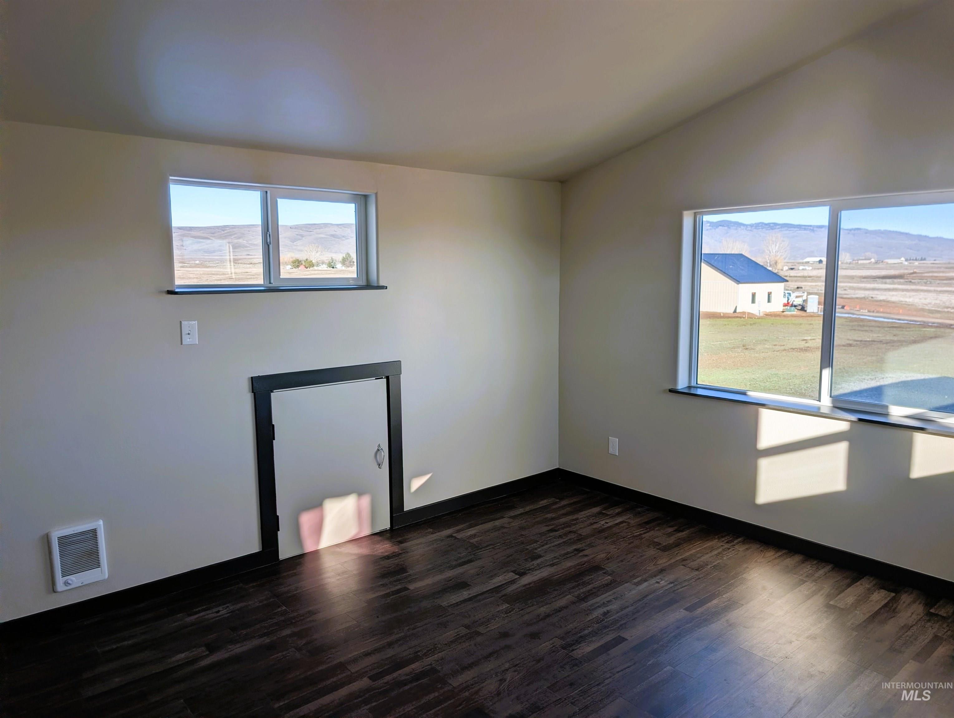 Spare room with dark wood-style floors, healthy amount of natural light, vaulted ceiling, and heating unit