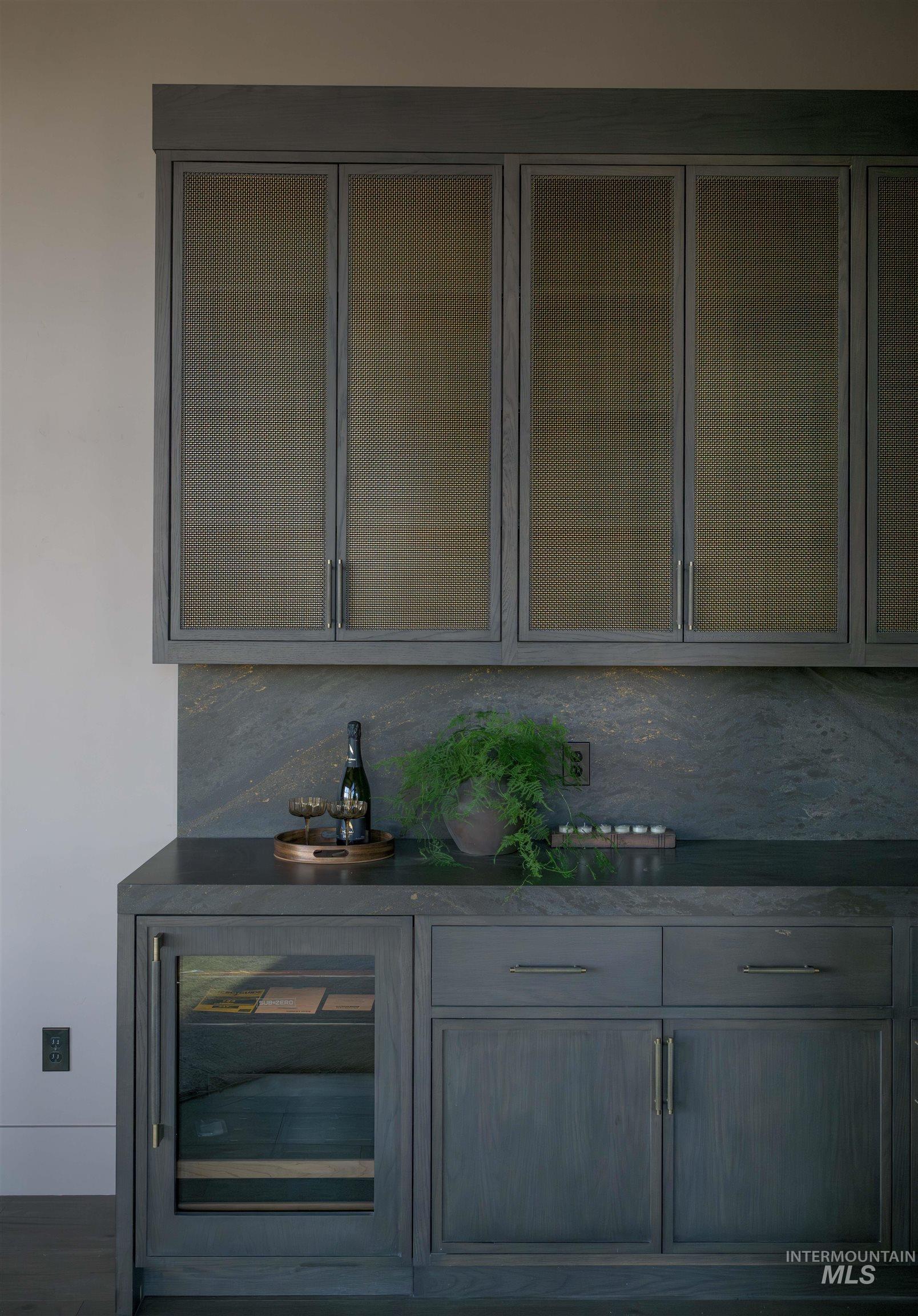 Indoor dry bar with beverage cooler, dark stone countertops, and gray cabinetry