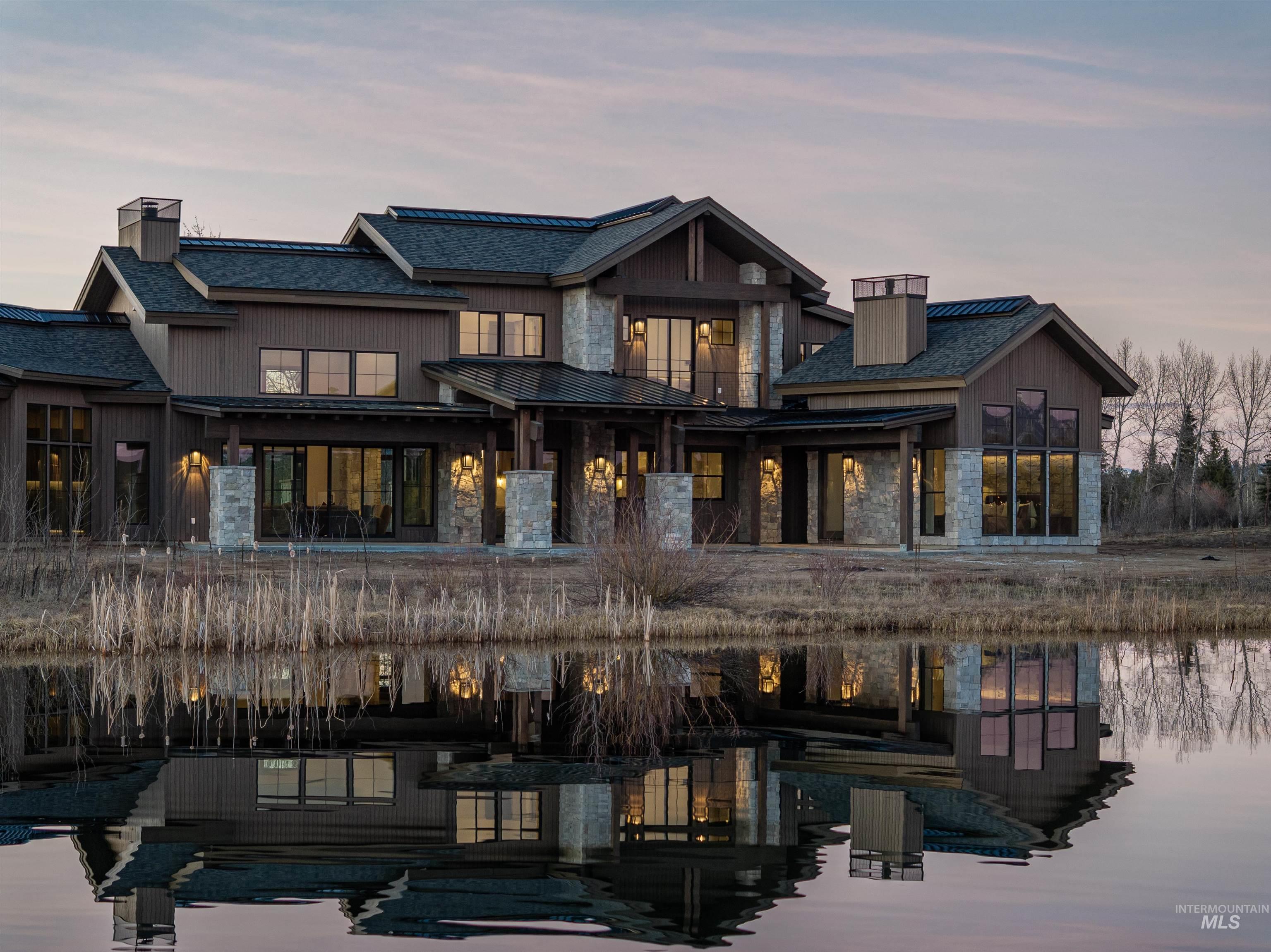Back of house at dusk featuring stone siding, a patio, a water view, and a chimney