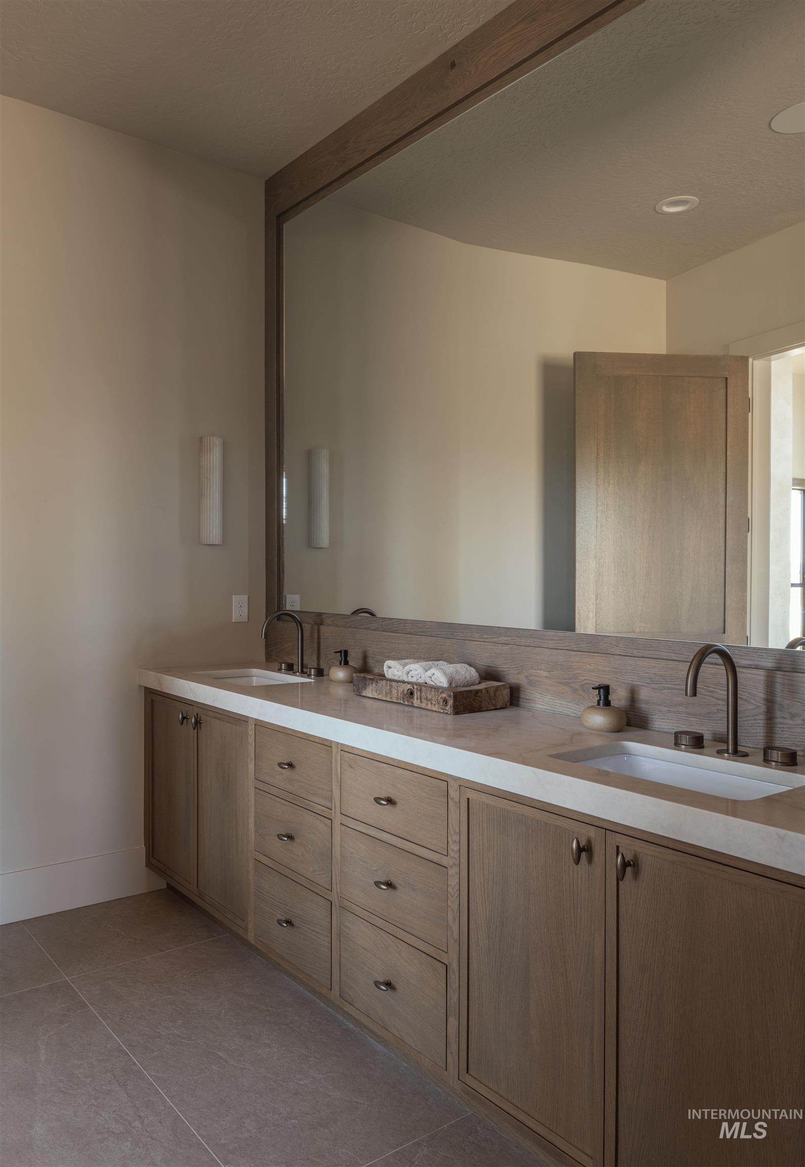 Primary Bathroom featuring double vanity, light tile patterned flooring, and a textured ceiling