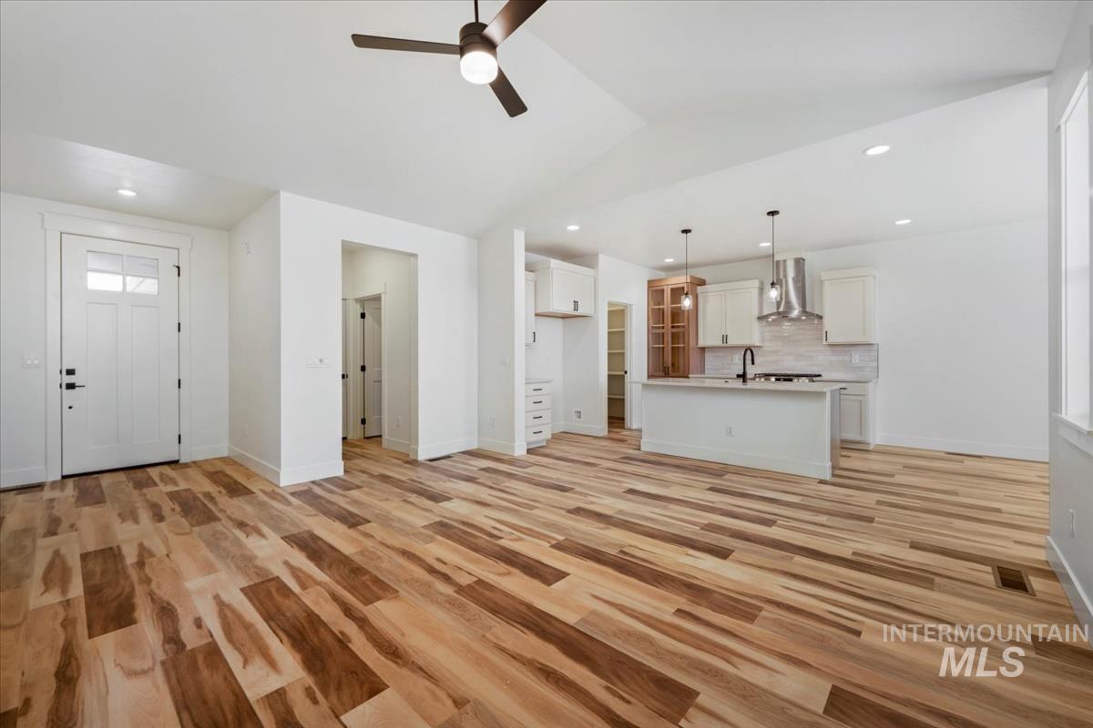 Unfurnished living room featuring a ceiling fan, light wood-type flooring, vaulted ceiling, and recessed lighting