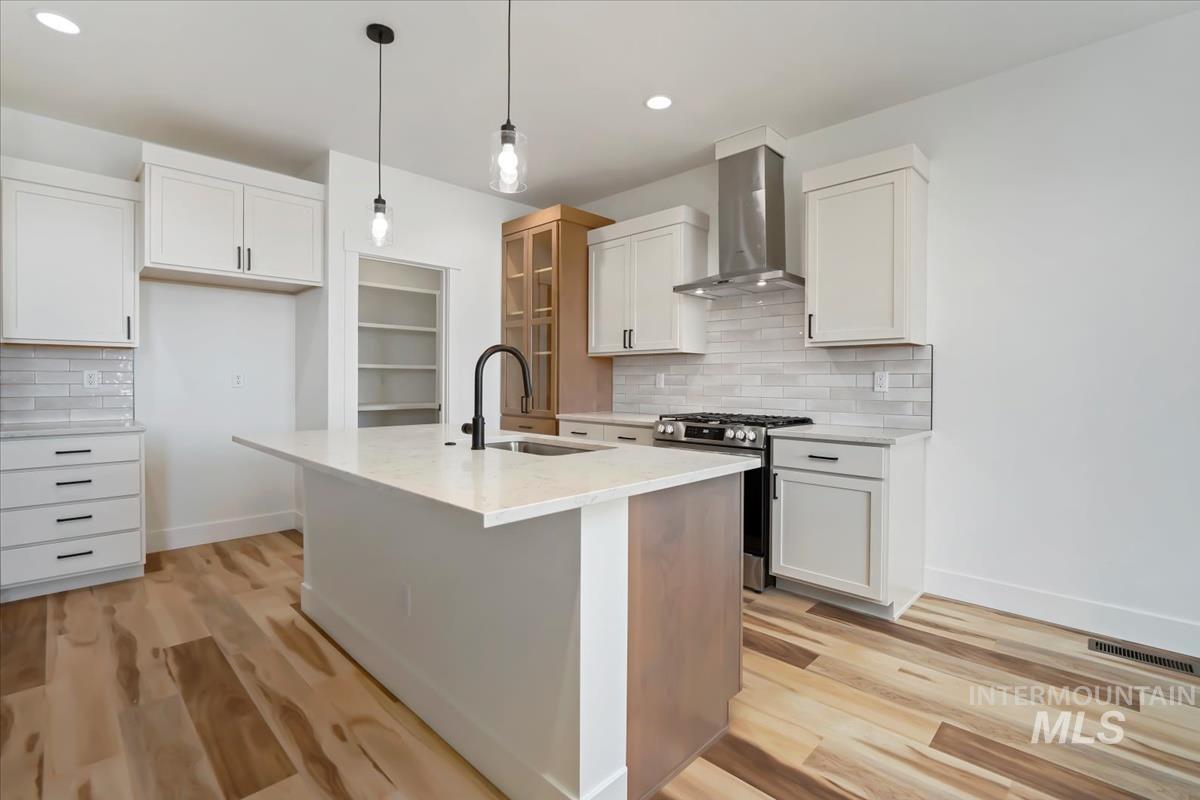 Kitchen with wall chimney exhaust hood, stainless steel range with gas stovetop, decorative backsplash, light wood finished floors, and recessed lighting