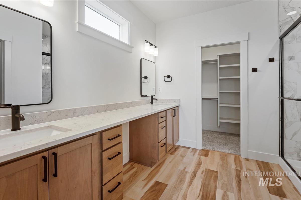 Full bathroom with a marble finish shower, double vanity, wood finished floors, and a walk in closet