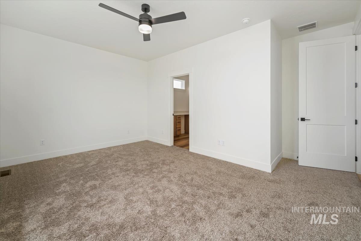 Carpeted empty room featuring a ceiling fan and a smoke detector
