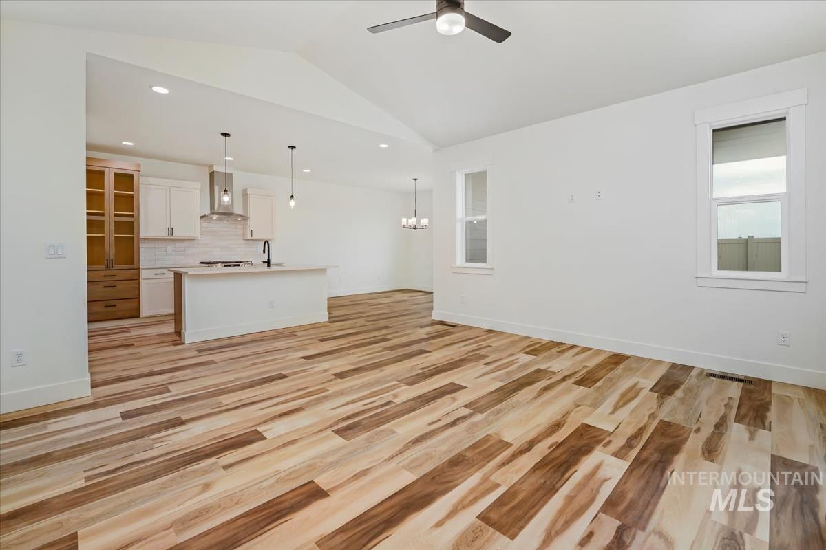 Unfurnished living room with lofted ceiling, ceiling fan, light wood finished floors, recessed lighting, and a chandelier