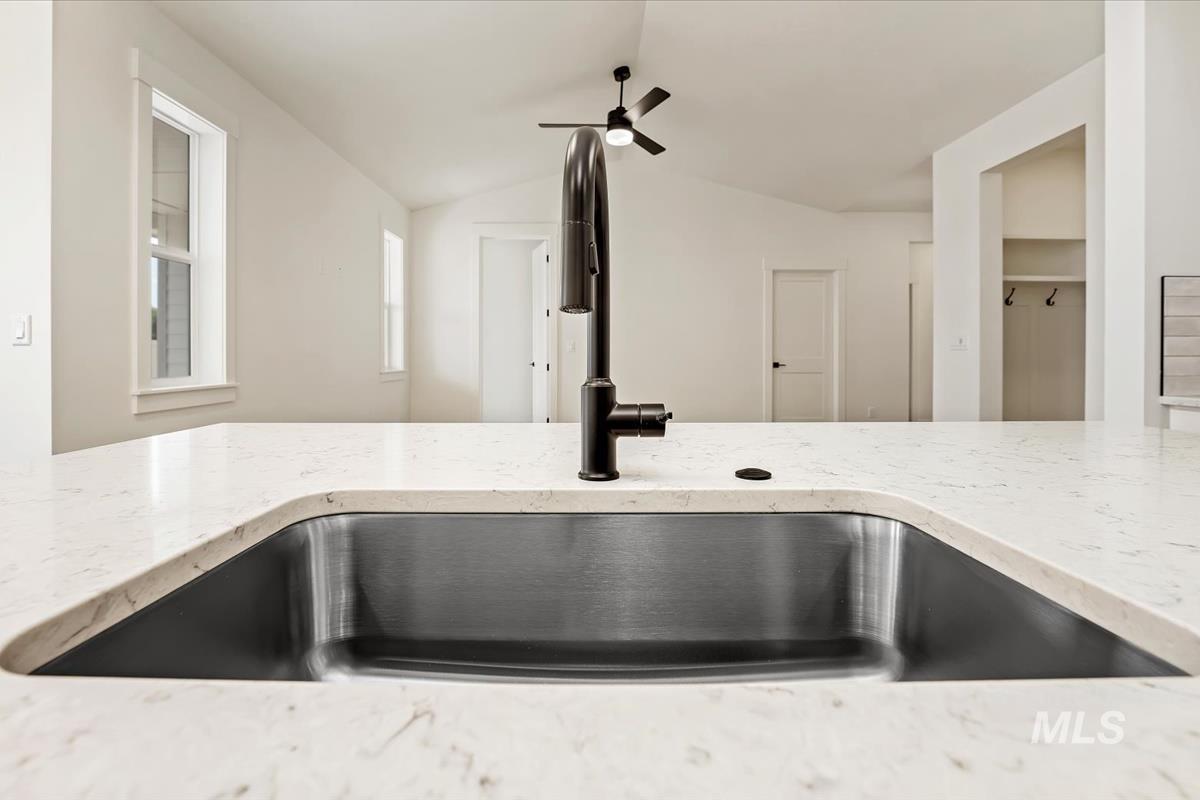 Kitchen view of light stone counters and a ceiling fan