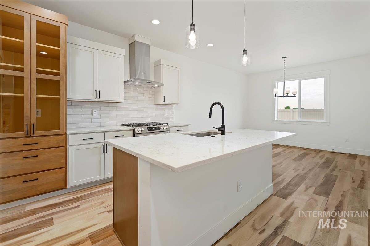 Kitchen with wall chimney range hood, a kitchen island with sink, white cabinetry, backsplash, and recessed lighting