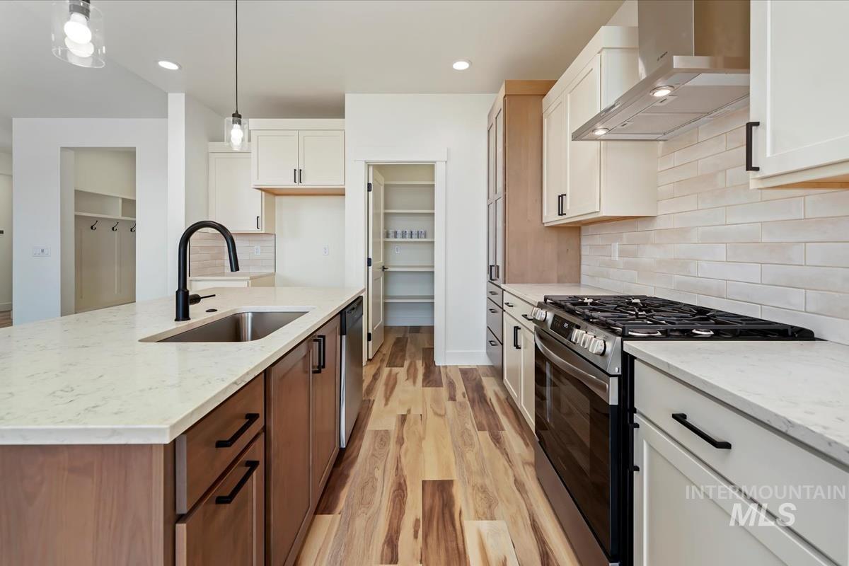 Kitchen featuring wall chimney exhaust hood, appliances with stainless steel finishes, light wood-style floors, white cabinets, and recessed lighting