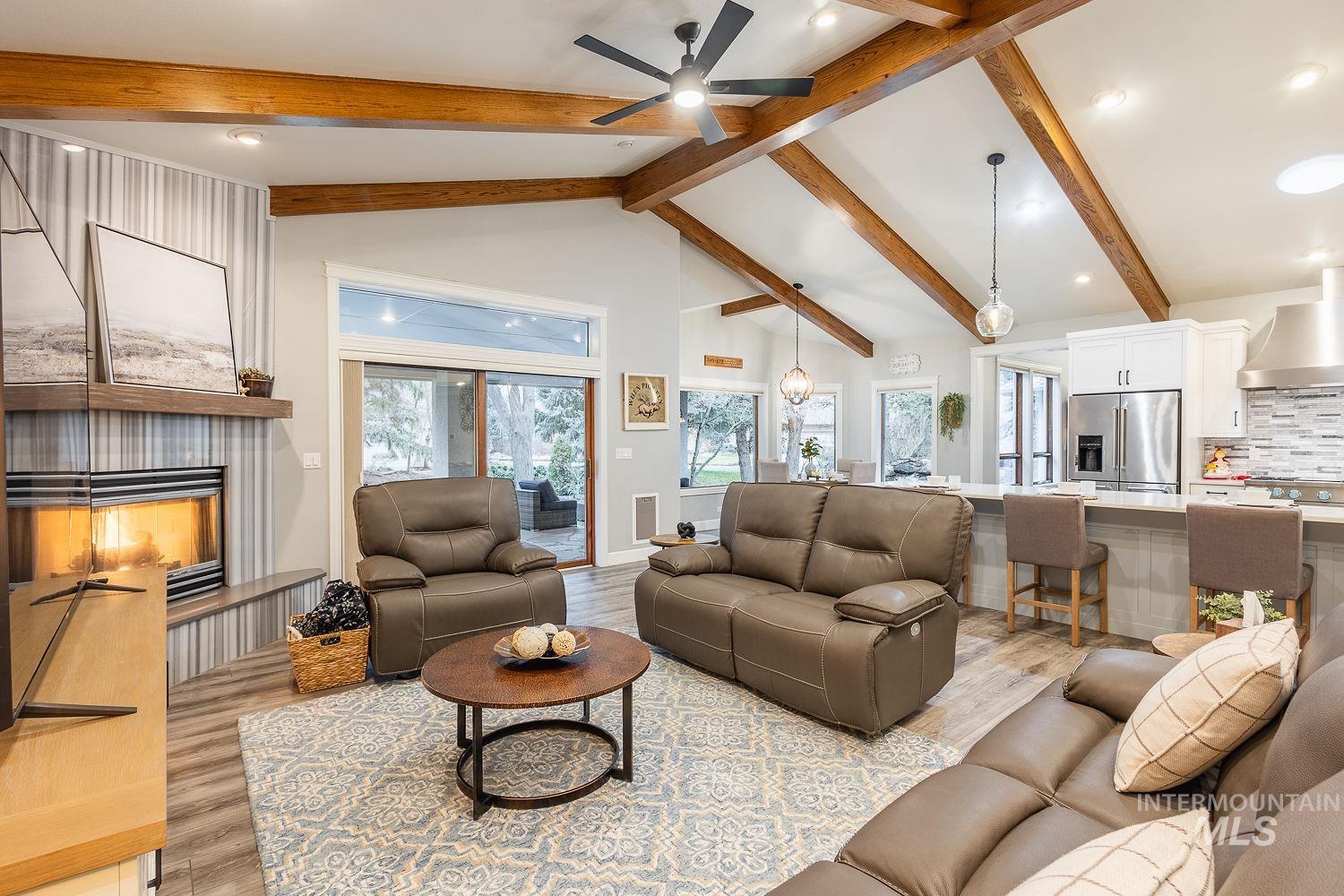 Living room with hanging lights, light wood-style floors, a ceiling fan, a fireplace, and vaulted ceiling
