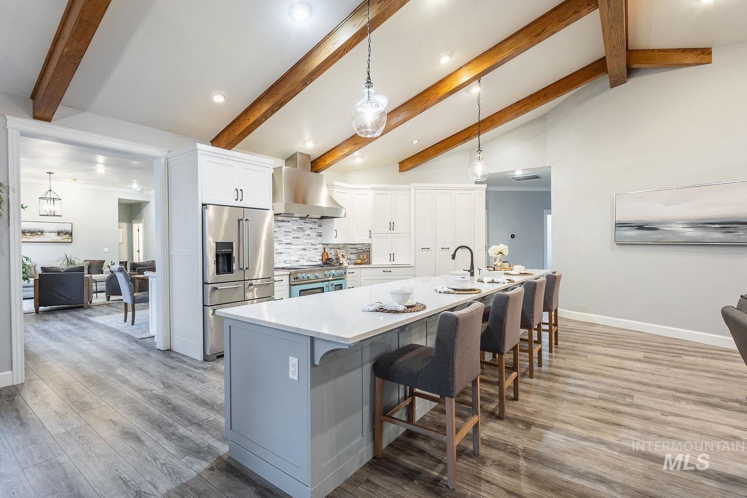 Two tone kitchen featuring premium appliances, a kitchen bar, light wood finished floors, hanging light fixtures, and vaulted ceiling with beams