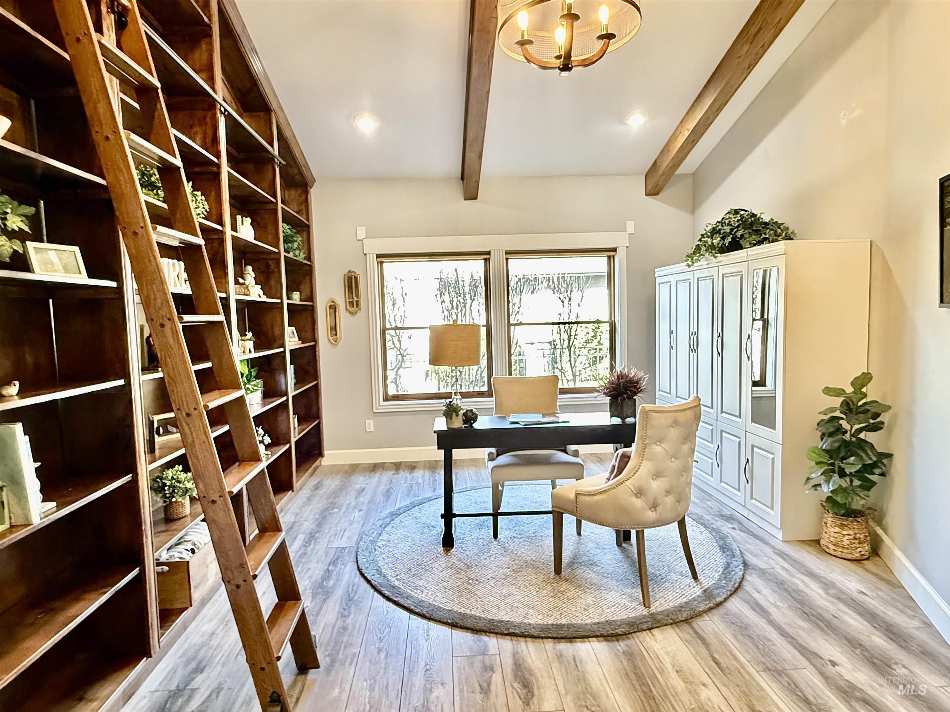 Home office or bedroom with light wood finished floors, hanging lights, and beam ceiling