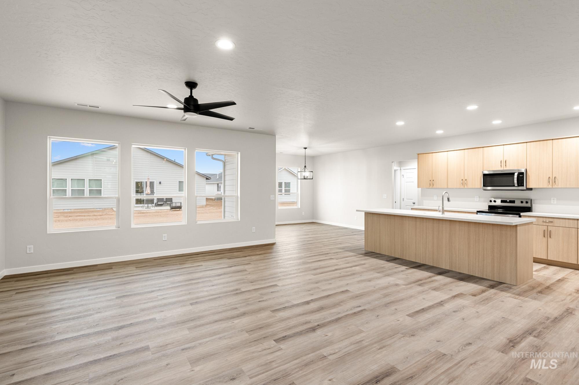 Kitchen featuring light brown cabinets, a kitchen island with sink, open floor plan, stainless steel appliances, and recessed lighting